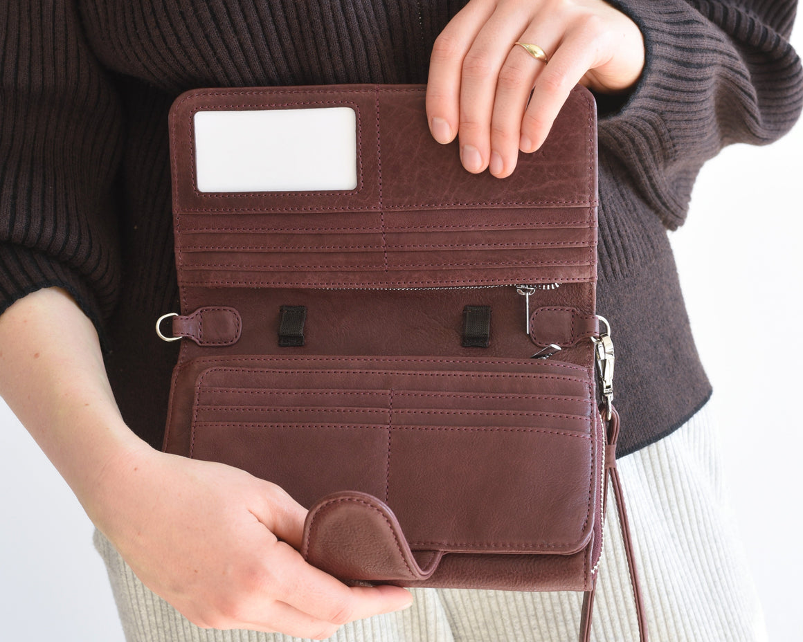 A dark reddish-brown leather wallet shown open, displaying its interior compartments, card slots, zipper pocket, and ID window, set against a clean white background with a decorative hexagonal tray partially visible on the right.