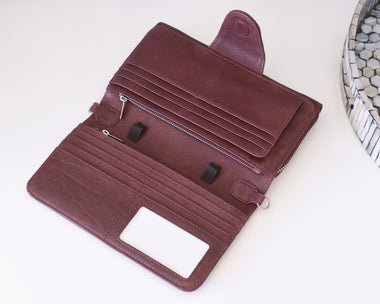 A dark reddish-brown leather wallet shown open, displaying its interior compartments, card slots, zipper pocket, and ID window, set against a clean white background with a decorative hexagonal tray partially visible on the right.