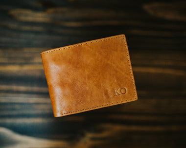 A tan brown leather wallet with a hot stamped monogram on a wooden background.