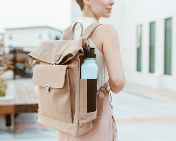 A person wearing a beige backpack with a blue water bottle attached to it, in an outdoor setting.