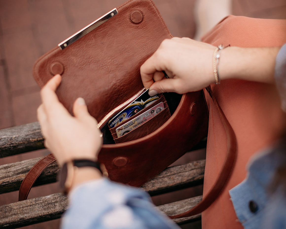 A model wearing a Caramel leather crossbody bag with a metal bar on the background of a large building