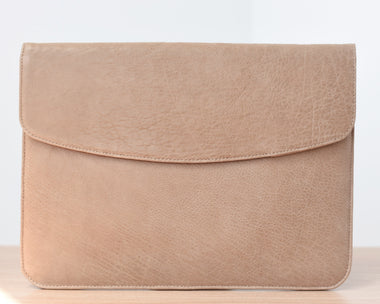 A light brown leather laptop sleeve with a suede lining, featuring a front pocket and a flap closure with magnetic locks.