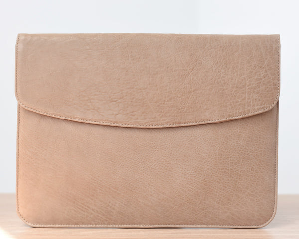 A light brown leather laptop sleeve with a suede lining, featuring a front pocket and a flap closure with magnetic locks.