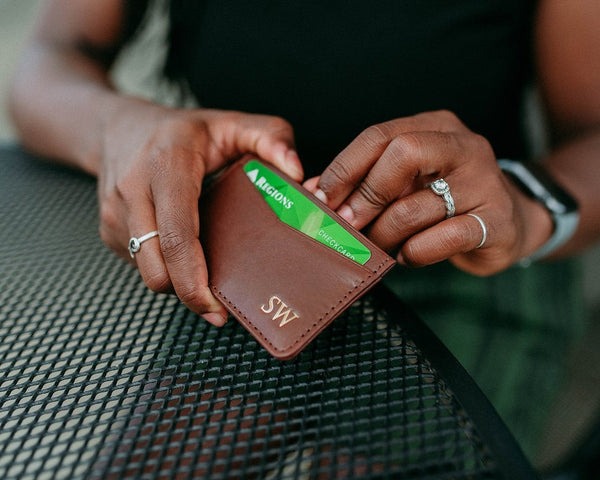 A person holding a brown leather card wallet with a green card slip-in pocket, situated at a table.