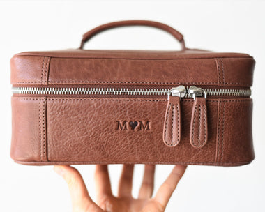 A brown leather toiletry bag with a zipper closure, a detachable zippered pouch on magnetic buttons, and a padded hand handle.
