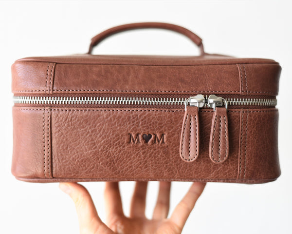 A brown leather toiletry bag with a zipper closure, a detachable zippered pouch on magnetic buttons, and a padded hand handle.