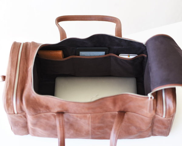 Large leather travel bag unzipped showing three interior pockets with accessories